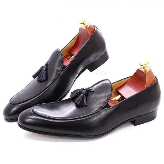 Black leather men's tassel dress loafers with wooden shoe trees on white background