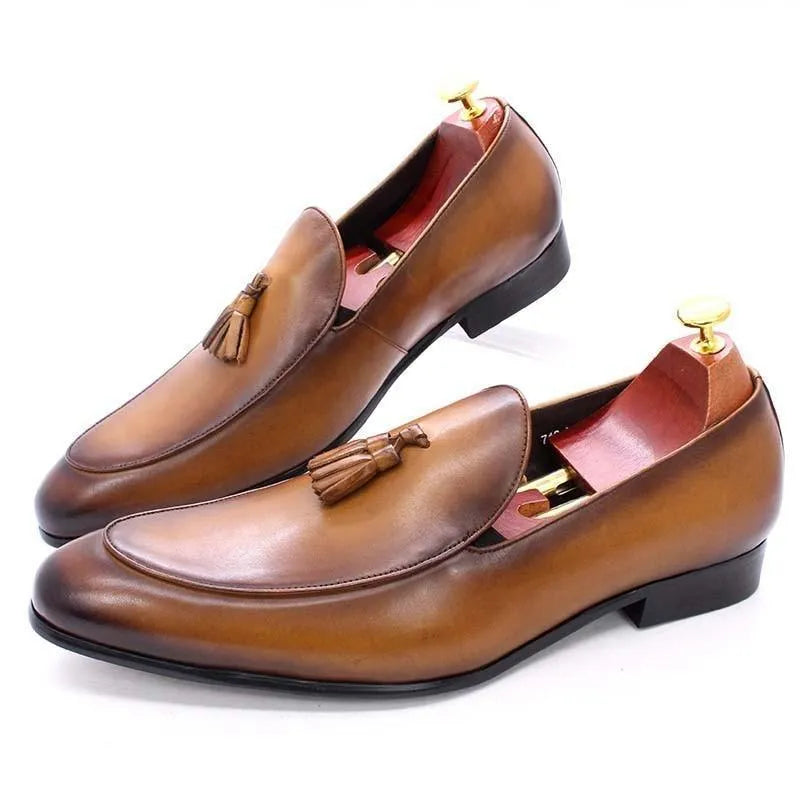 Brown leather tassel dress loafers for men with wooden shoe trees on white background
