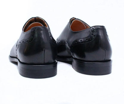 Black leather men's dress shoes with brogue detailing, rear view on white background