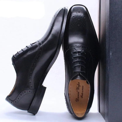 Black leather lace-up men's dress shoes with brogue detailing on a light background