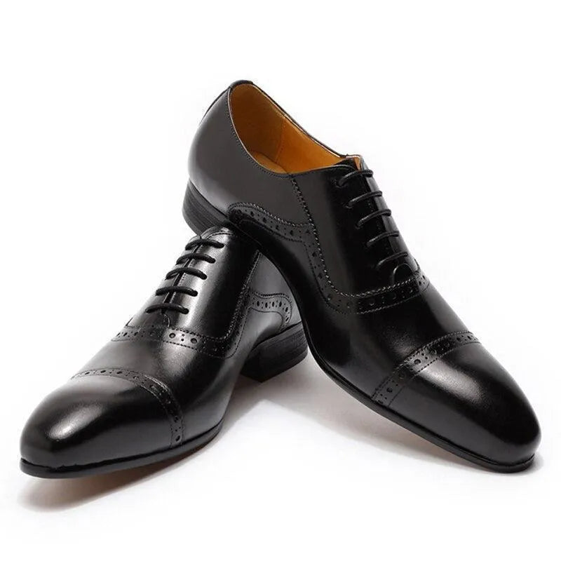 Black leather men's dress shoes with pointed toe and brogue detailing on a white background