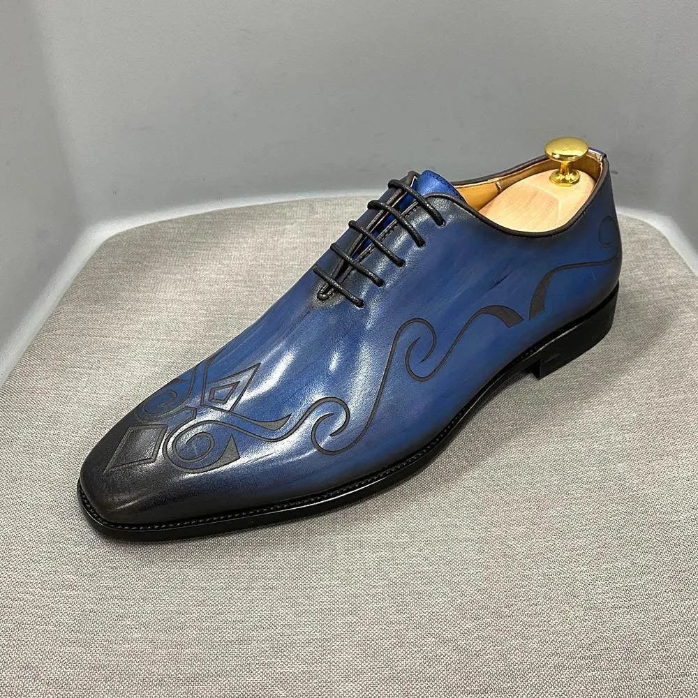 Blue classic men's leather dress shoe with black swirl pattern, displayed on gray fabric.