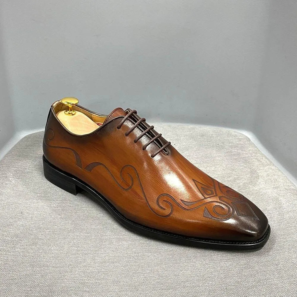 Brown leather men's dress shoe with black decorative patterns on gray background