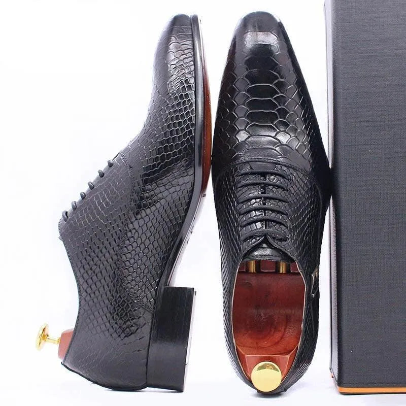 Black men's dress shoes with lizard skin texture and wooden shoe trees on white background