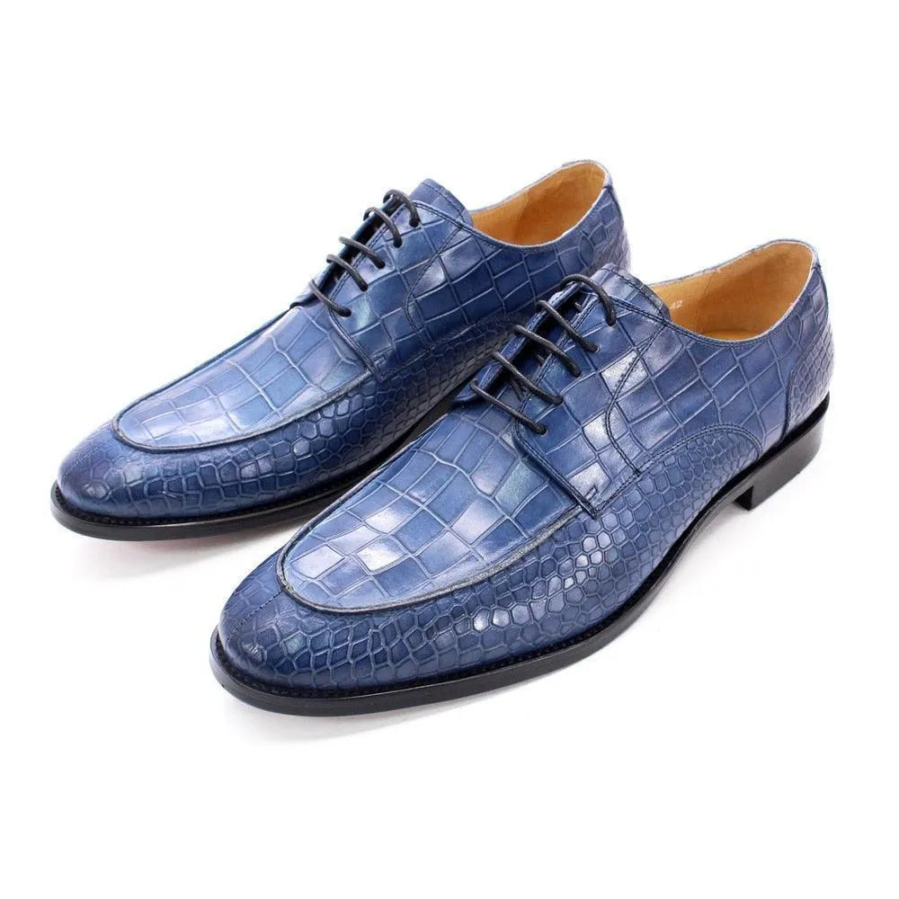 Blue crocodile pattern men's dress shoes with black soles on white background