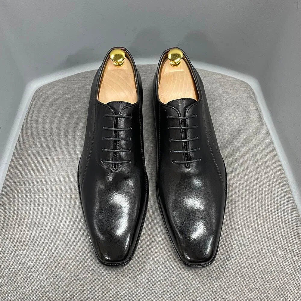 Black leather men's dress shoes with wooden shoe trees on a gray chair