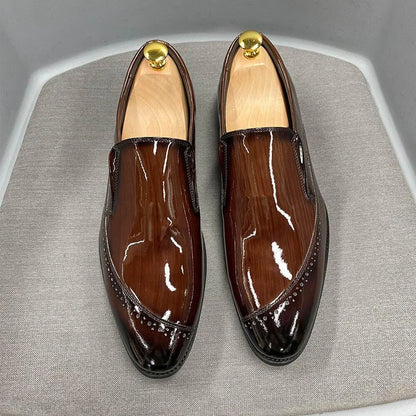 Glossy brown men's dress slip-on shoes with brogue detail displayed on a gray surface