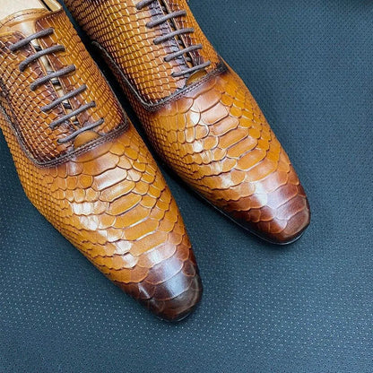 Brown men's dress shoes with snake skin texture on a dark textured surface