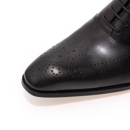 Black leather men's dress shoe with brogue detailing on white background