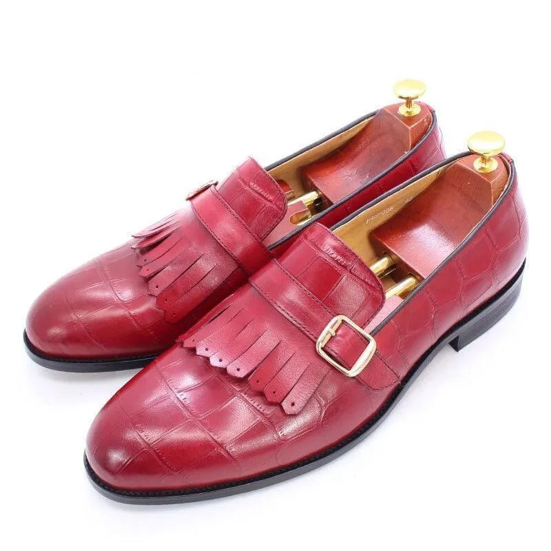 Red leather men's dress shoes with fringe detail and gold buckles on white background