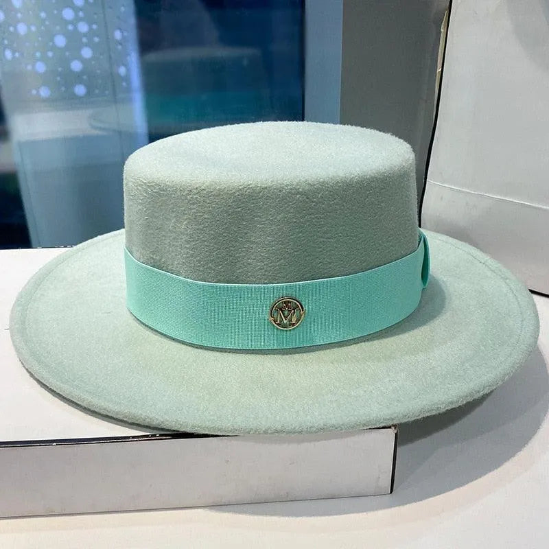 Light blue flat top fedora hat for women with ribbon and gold emblem on a display box