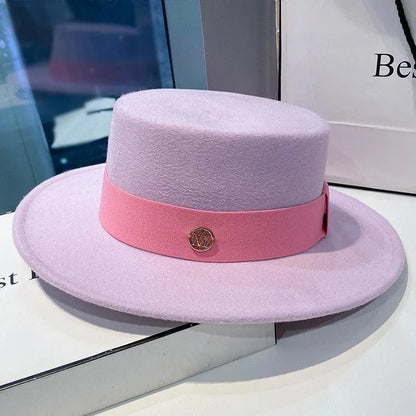 Elegant women's lavender flat-top fedora hat with pink band and gold accent, displayed indoors.